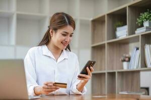 Beautiful young Asian woman holding smartphone and using credit card for online shopping. photo