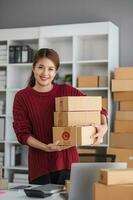 Starting small business entrepreneur of independent Asian woman smiling using computer laptop with cheerful success of online marketing package box items and SME delivery concept photo