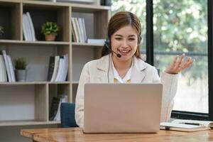 Asian call center with headset and microphone working on her laptop. Female operator provide exceptional customer service. Supportive call center agent helping customer on inquiry. Enthusiastic photo