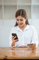 Beautiful young Asian woman holding smartphone and using credit card for online shopping. photo