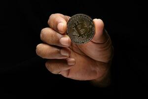 Asian male dark skinned single hand fist finger on black background holding golden fake sample physical bitcoin cryptocurrency photo