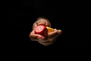 Asian male dark skinned single hand fist finger on black background holding wooden red yellow playing dice photo