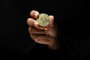 Asian male dark skinned single hand fist finger on black background holding golden fake sample physical bitcoin cryptocurrency photo