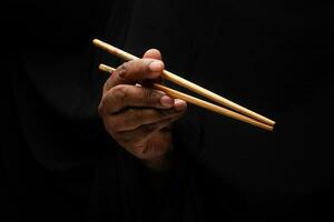 Asian male dark skinned single hand fist finger on black background holding chopsticks feed eat photo