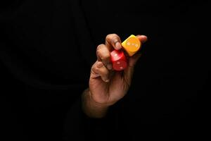 Asian male dark skinned single hand fist finger on black background holding wooden red yellow playing dice photo