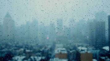 Rain drops pouring down on window glass with urban city skyline view on a rainy weather day video