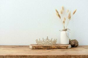 Stylish composition of table with beads and flowers and crown, bench in retro style, clay vases and crockery. Rustic inspiration. Summer vibes. Beige wood table. photo