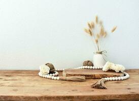 Stylish composition of table with beads and flowers and crown, bench in retro style, clay vases and crockery. Rustic inspiration. Summer vibes. Beige wood table. photo