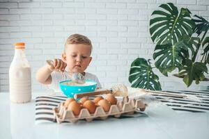 A little boy kneads the dough with a whisk. The child prepares the dough for pancakes. Little cook. photo