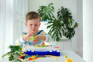 Little boy playing set with a screwdriver and a drill,  and screws and parts . The child plays builder with a toy drill to develop imagination and motor skills. Educational logic toys for children. photo