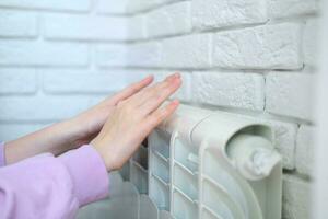 el niño es manos calentar su manos cerca el calefacción radiador. ahorro gas en el calefacción estación. foto