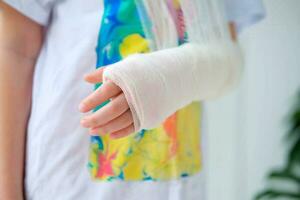 Close-up of a broken arm of a child in a cast. The girl holds her hand folded against the background of a multi-colored T-shirt.A child with a plaster on his hand photo