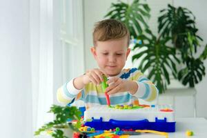 Little boy playing set with a screwdriver and a drill,  and screws and parts . The child plays builder with a toy drill to develop imagination and motor skills. Educational logic toys for children. photo