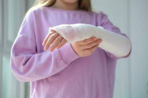 Close-up of a broken arm of a child in a cast. The girl holds her hand folded against. A child with a plaster on his hand photo