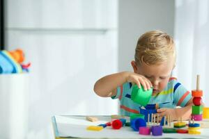 un pequeño chico obras de teatro con de madera juguetes y construye un torre. educativo lógica juguetes para niños. montessori juegos para niño desarrollo. para niños de madera juguete. foto