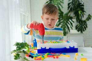 Little boy playing set with a screwdriver and a drill,  and screws and parts . The child plays builder with a toy drill to develop imagination and motor skills. Educational logic toys for children. photo