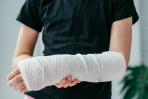 Close-up of a broken arm of a child in a cast. The girl holds her hand bent on the background of a black t-shirt. photo