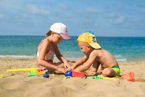 hermano y hermana jugar en el playa con el plastico juguetes con arena.niños son jugando en el playa. verano agua divertido para el todo familia. un chico y un niña son jugando con arena en el costa. foto