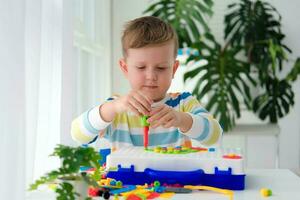 Little boy playing set with a screwdriver and a drill,  and screws and parts . The child plays builder with a toy drill to develop imagination and motor skills. Educational logic toys for children. photo