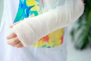 Close-up of a broken arm of a child in a cast. The girl holds her hand folded against the background of a multi-colored T-shirt.A child with a plaster on his hand photo