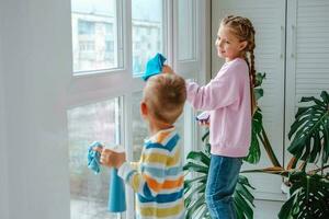 Little boy and girl sprinkles water from a bottle on the window and wipes it off with a rag. The children helps with cleaning the house. Clean the window. Brother and sister busy cleaning. photo