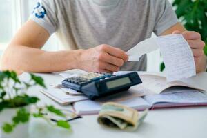 un hombre cuenta un cuenta en un calculadora en el mesa. pago de utilidad servicios. ahorro energía y dinero concepto. foto