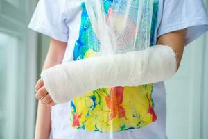 Close-up of a broken arm of a child in a cast. The girl holds her hand folded against the background of a multi-colored T-shirt. A child with a plaster on his hand photo