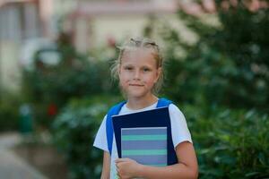 retrato de un niña con un maletín y cuadernos en su manos en el calle. espalda a escuela. foto