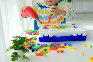 pequeño chico jugando conjunto con un destornillador y un perforar, y empulgueras y partes . el niño obras de teatro constructor con un juguete perforar a desarrollar imaginación y motor habilidades. educativo lógica juguetes para niños. foto