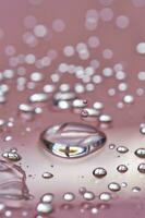 A large drop and splashes of micellar water on a pink background. photo