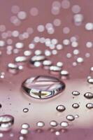 A large drop and splashes of micellar water on a pink background. photo