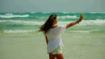 un' ragazza prende un' autoscatto su un' bellissimo spiaggia, pose con un' smartphone video