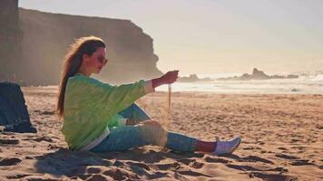 un' ragazza si siede su il spiaggia nel il raggi di il sole a tramonto video