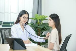 Asian female doctor in uniform holding a stethoscope and using it to measure the heart rate of an asian female patient with heart disease photo