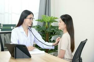 Asian female doctor in uniform holding a stethoscope and using it to measure the heart rate of an asian female patient with heart disease photo