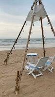 ein hölzern Tipi Stil mit ein einstellen von Tabellen und Stühle auf das Strand. video