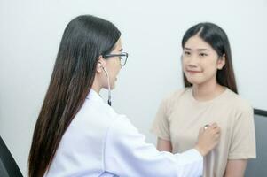 asiático hembra médico en uniforme participación un estetoscopio y utilizando eso a medida el corazón Velocidad de un asiático hembra paciente con corazón enfermedad foto