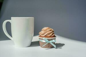 A cupcake or muffin stands next to a cup of coffee. photo
