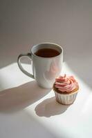 A cupcake or muffin stands next to a cup of coffee. photo