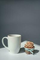 A cupcake or muffin stands next to a cup of coffee. photo