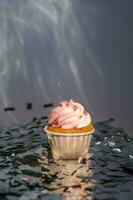 A cupcake with a pink cap stands among the flying silver confetti. photo