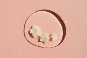 A drop of transparent cosmetic gel with flower on a pink background. photo