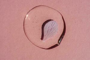 A drop of transparent cosmetic gel with flower on a pink background. photo
