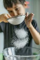 The child cooks in the kitchen. Sifts the flour. photo