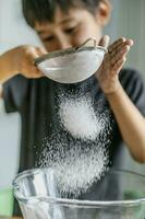 The child cooks in the kitchen. Sifts the flour. photo