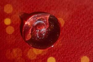 A drop of serum on a red background with bokeh. photo