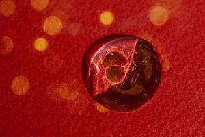 A drop of serum on a red background with bokeh. photo