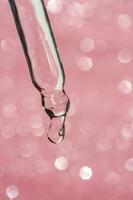 Cosmetic pipette with a drop on pink background. photo