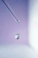 A drop of cosmetic oil falls from the pipette on a purple floral background. photo