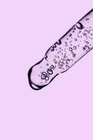 transparente pipeta con productos cosméticos en un púrpura antecedentes. foto